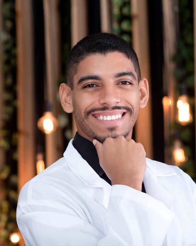 Victor Hugo Sales Santos de jaleco branco, sorrindo, com a mão no queixo
