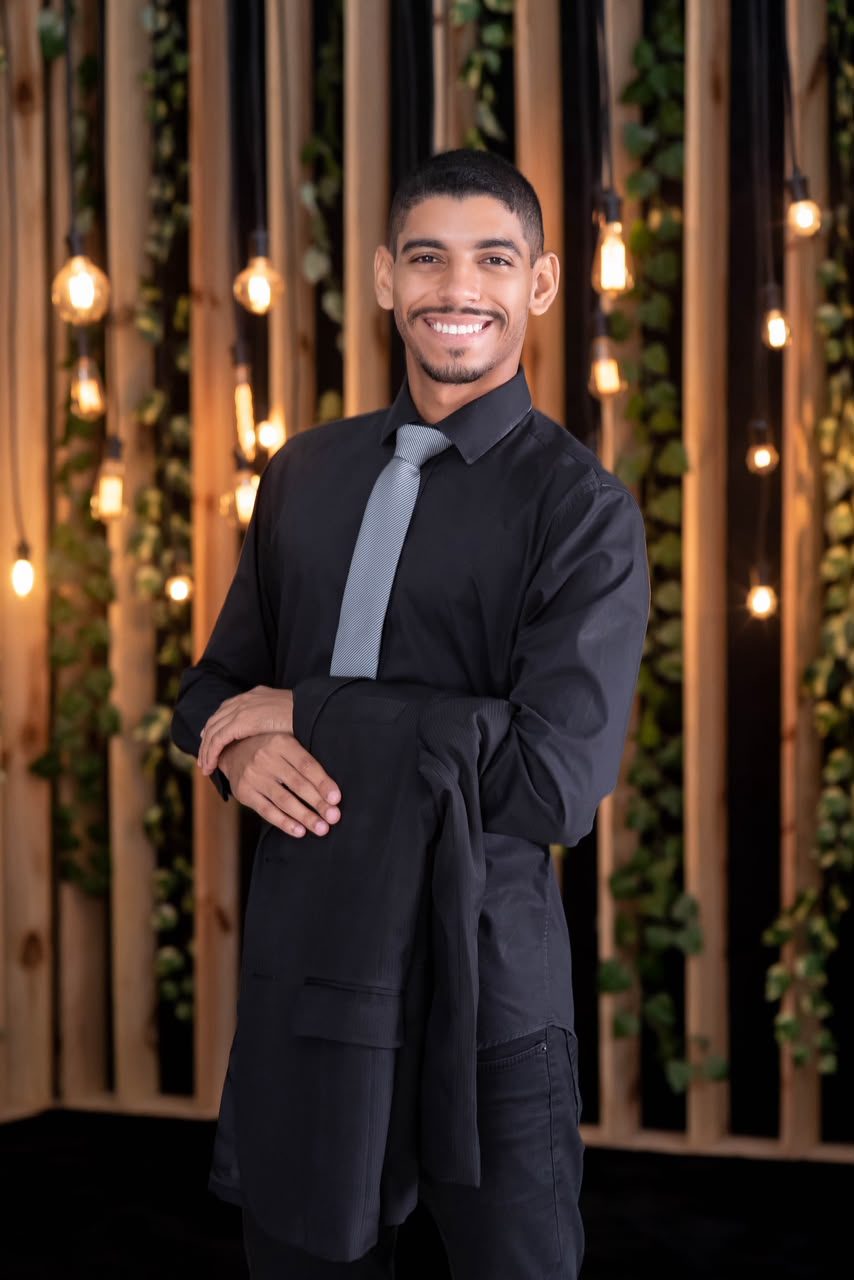 Victor Hugo Sales Santos sorrindo, de camisa e gravata, segurando o paletó